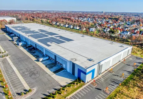 Aerial view of a large distribution center with a solar-panel roof and loading docks, autumn suburb in the background