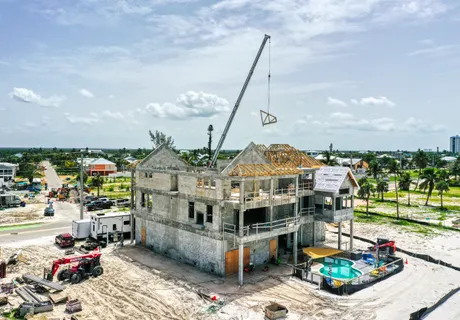 Aerial photo of a concrete-shell home under construction on Fort Myers Beach, crane on site and framing in progress after Hurricane Ian
