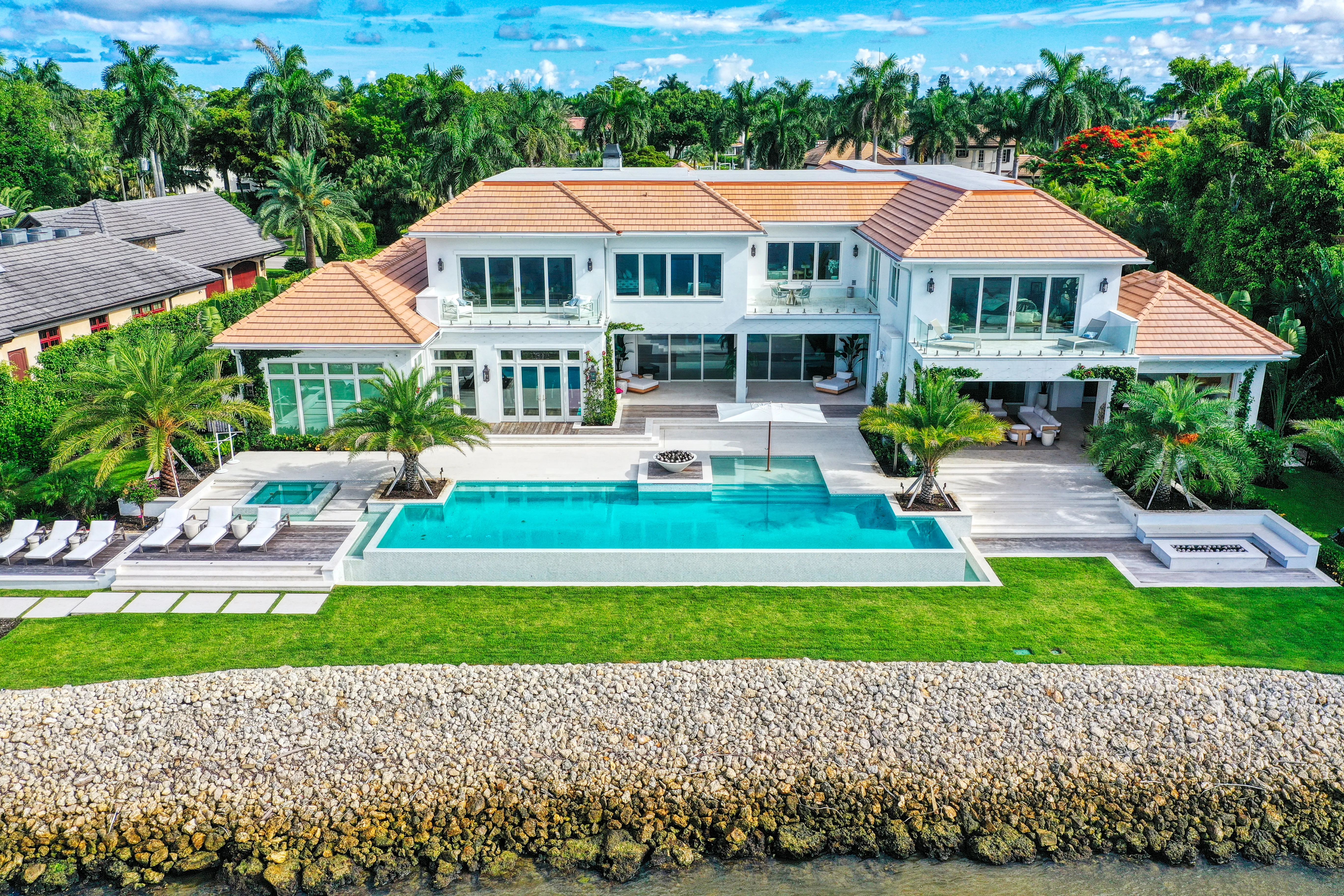 Aerial view of a luxury waterfront estate in Naples with an infinity pool and manicured lawn running down to the seawall