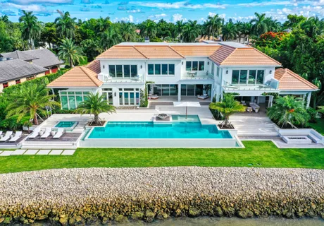 Aerial view of a luxury waterfront estate in Naples with an infinity pool and manicured lawn running down to the seawall