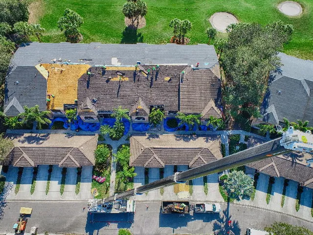 Aerial view of a roof mid tear-off with crew and materials staged during a re-roofing job.