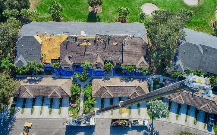 Aerial of an active re-roof in progress with tear-off and a material lift