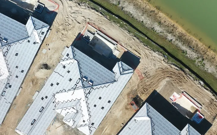 Top-down aerial of a lakeside community mid-build, homes framed on bare graded lots