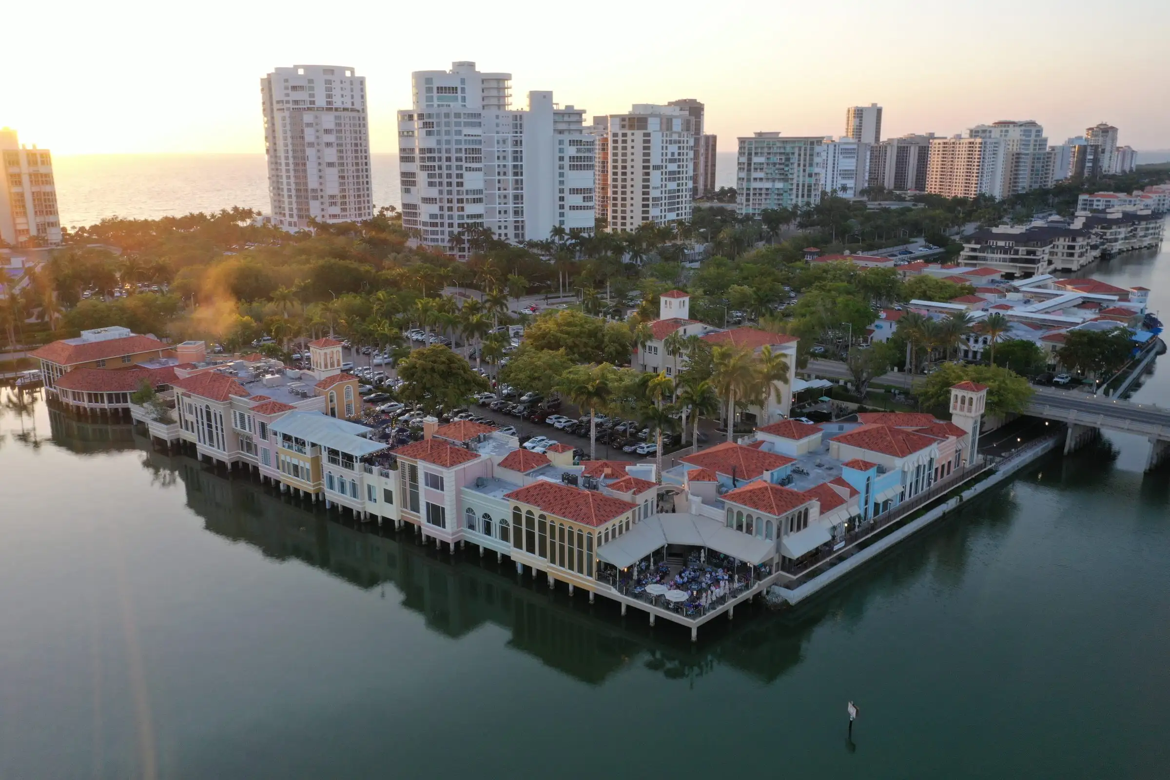 Sunset over a waterfront shopping village built out over the bay, with condominium towers behind it